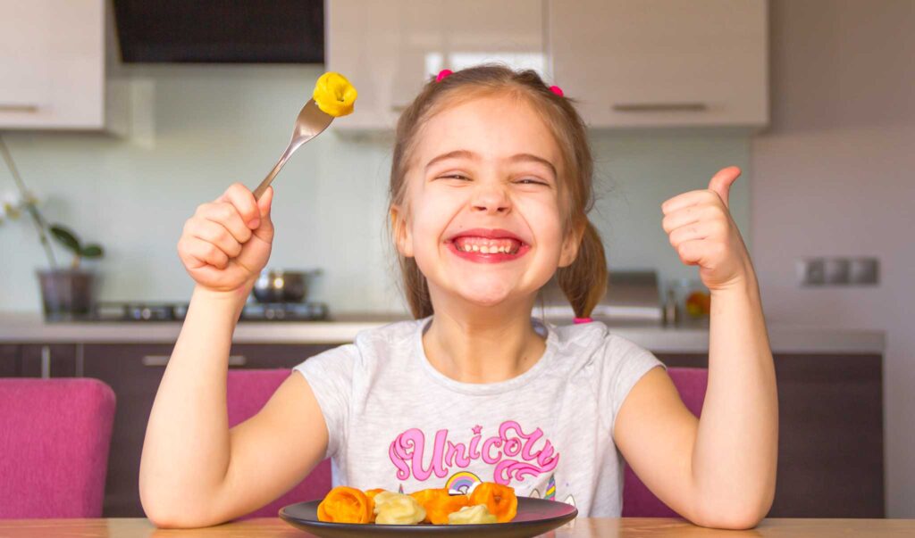easy kid friendly dinner recipes  represented by a young girl smiling and giving a thumbs up while eating