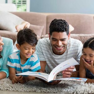 important benefits of reading to children represented by parents and young children reading together lying on a floor rug in their living room