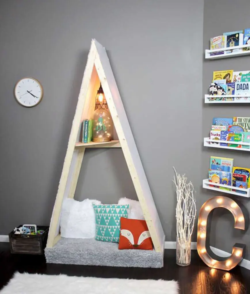 Indoor reading nook tent with gray floor cushion, and fox and other throw pillows, with shelves filled iwth kids books on the other wall.