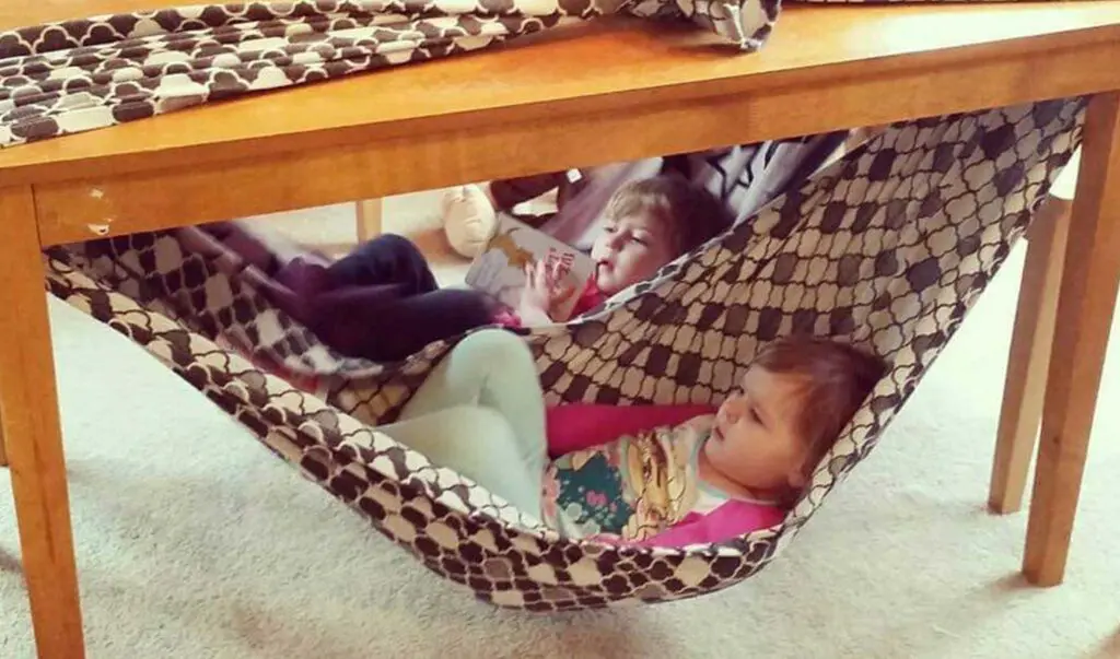 Two young children lying in hammocks made from sheets tied on a table