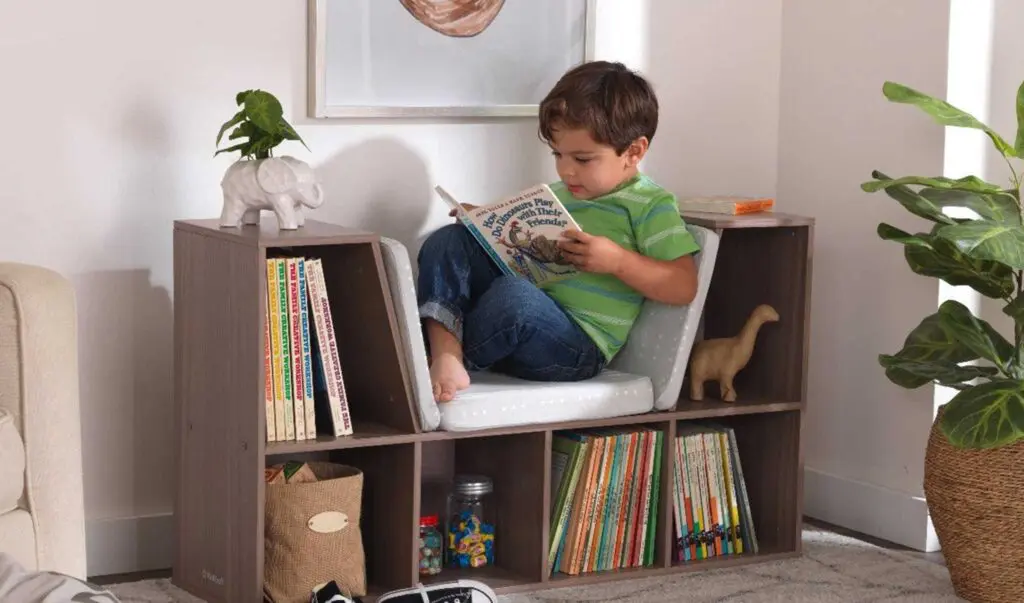 Young boy reading a book while sitting in a bookcase nook