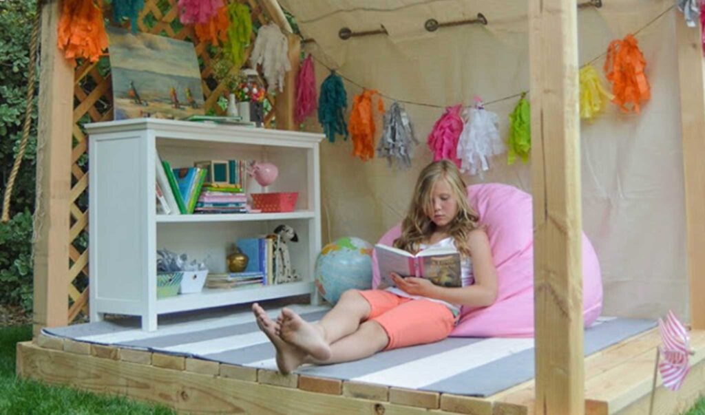 Tween girl reading a book in a DIY outdoor reading nook hut.